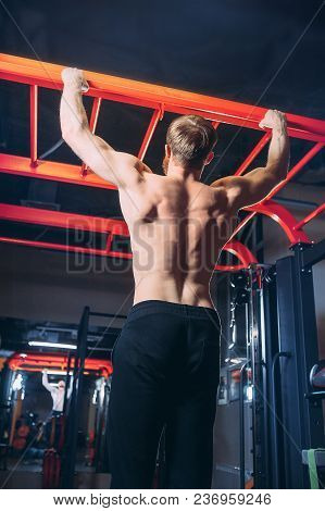 Black And White Image Of Power Muscular Bodybuilder Guy Doing Pullups In Gym. Fitness Man Pumping Up