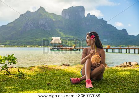 Bora Bora tourist woman relaxing on beach drinking fresh coconut water by Otemanu mount in landscape. French Polynesia travel vacation.