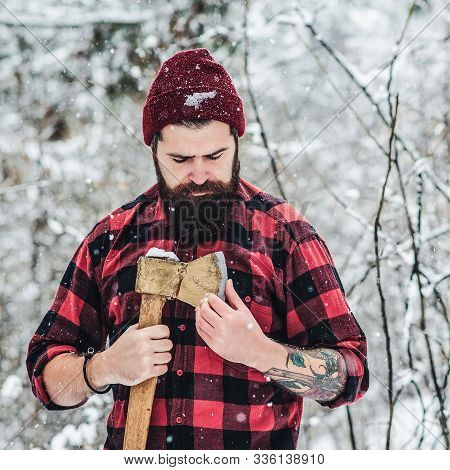 Bearded Hipster Checks Ax Blade In Winter Forest. Lumberjack Works In Snowy Day. Bearded Guy Wears C