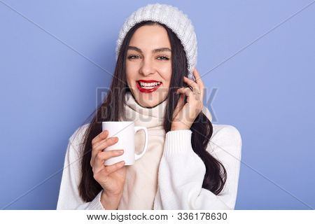 Young Attarctive Woman Holding Cap Ofhot Beverage In Her Hands, Wearing White Warm Sweater, Scarf An