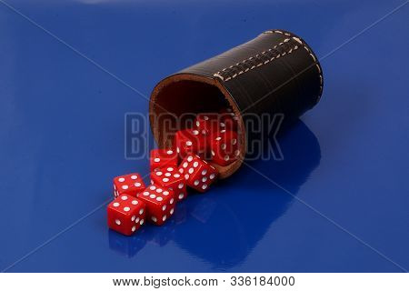 Red Dice Falling Out Of A Leather Dice Cup On A Blue Background In The Studio