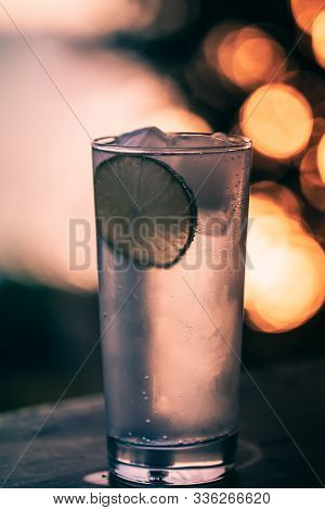 Cocktail Glass With Gin Tonic And A Lime And Ice Cubes On A Balcony With Scenic And Magnificent View
