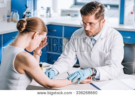 Selective Focus Of Handsome Allergist Holding Ruler Near Marked Hand Of Sad Woman