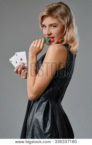 Blonde Girl In Black Dress Holding Two Playing Cards And Green Chips, Posing Sideways Against Gray B