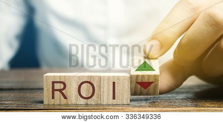 Wooden Blocks With The Word Roi And Green Arrow Up. High Level Of Business Profitability. Return On 