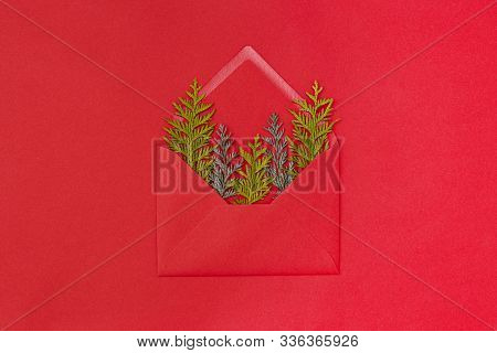 An Envelope With Green Spruce Branches On The Red Paper Background. Chrictmas Concept