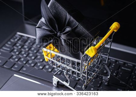 Black Friday Concept. Yellow Trolley With Gift And Laptop Against A Dark Background .