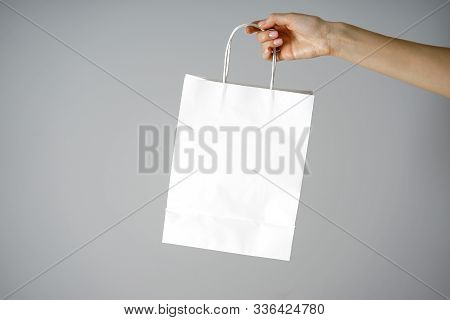 Paper White Craft Bag, Eco Packaging In A Female Hand, On A Gray Background, With Place For Text. Sa
