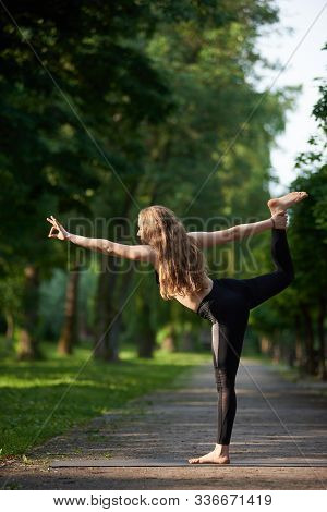 Woman With Long Hair In Black Sports Suit Standing In Pose Of King Of Dance, Asan Natarajasana, Agai