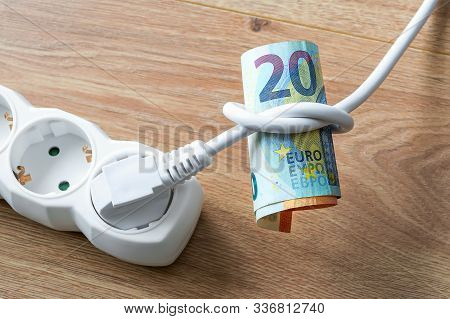 White Electric Cable With Plug Tied To A Knot On A Roll Of Euro Banknotes. Cost Of Electricity And E