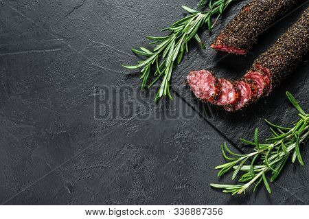 Fuet, Salami And A Sprig Of Rosemary. Traditional Spanish Sausage. Black Background. Top View. Space
