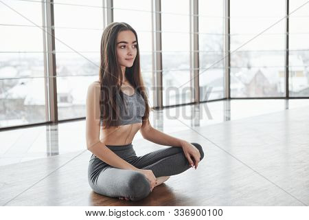Relaxed Cute Young Girl Sits On The Floor In Gym With Big Windows.