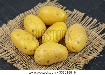 Group Of Six Whole Pale Yellow Potato On Natural Sackcloth On Grey Stone