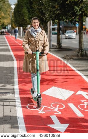 traffic, city transport and people concept - happy smiling woman riding electric scooter along red bike lane with signs of bicycles and two way arrows on street