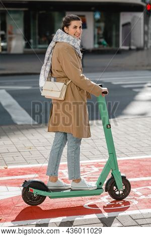 traffic, city transport and people concept - happy smiling woman riding electric scooter along red bike lane with signs of bicycles and two way arrows on street