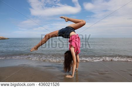Young Girl Does A Spin And Reverse Wheel During Exercises By The Sea In The Summer