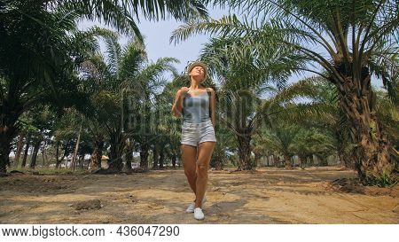 Woman Tourist With Plait Walks Looking Around At Growing Young Trees With Lush Leaves At Oil Palm Fa