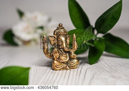 Bronze Ganapathi Ganesha Idol Decorated With White Flowers And Green Leaf In Background