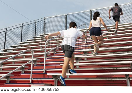 Rear View Of Young Runners Running Up Red Stadium Bleachers At A Pre Season Running Summer Camp.