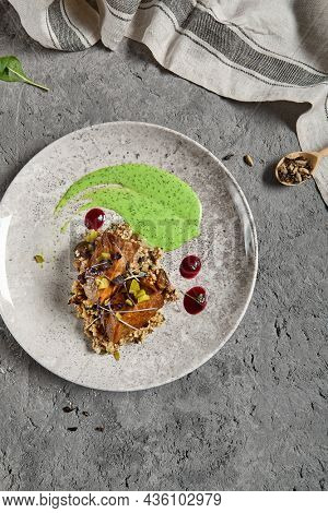 Roasted beef tongue with green buckwheat and green sauce. Main course with beef tongue and garnish on gray stone table. Aesthetic composition with meat dish and textile. Beef in restaurant menu