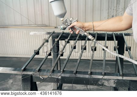 Woman Worker Paints Forged Balusters In Black Color With Spray Gun On Rack Support In Contemporary S
