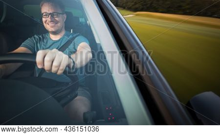 Handsome young driver driving hic car fast yet safely on the road (motion blurred image)
