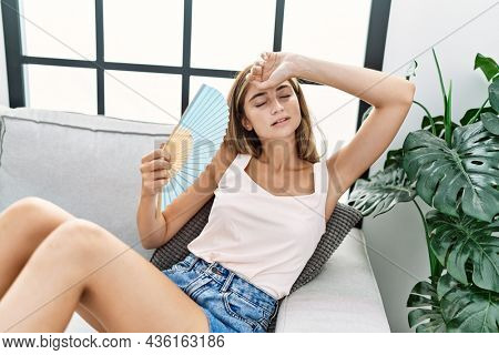 Young caucasian woman using handfan at home