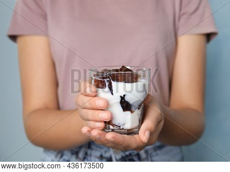 Woman Holding Glass Of Milk With Delicious Grass Jelly On Light Blue Background, Closeup