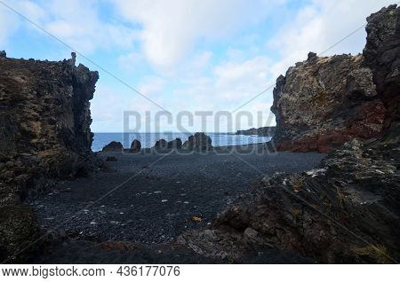 Large Black Lava Rock Cliffs On A Black Sand Beach.