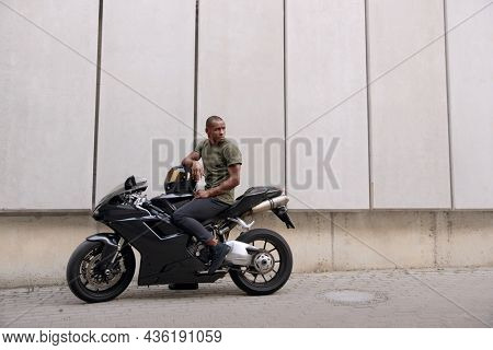 Young black man sitting on sports motorcycle on city street. Guy wearing casual clothes. Concept of trip and journey in personal transport. Vacation, leisure, hobby and enterteiment. Idea of freedom.