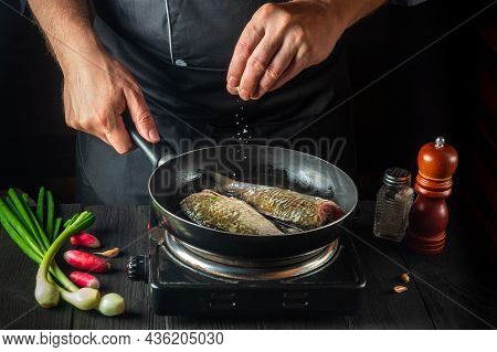 Chef Prepares Fresh Fish In Pan Sprinkling Salt With The Ingredients. Preparing To Cook Fish Food. W