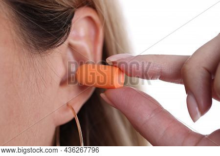 Woman Inserts Orange Earplugs Into Ears Closeup