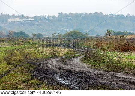 Autumnal Foggy Morning Rustic Lansdcape With Dirt Road In The Foreground And Small Buildings On Hill