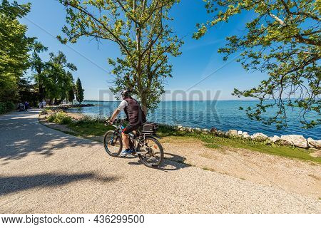 Lazise, Italy - May 26, 2021: Coast Of Lake Garda With A Beach And Bicycle And Pedestrian Lane That 