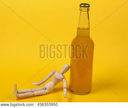 Alcoholism. Wooden Puppet And Bottle Of Beer On Yellow Background.