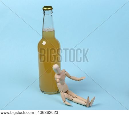 Alcoholism. Wooden Puppet And Bottle Of Beer On Blue Background.