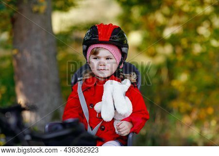 Little Toddler Girl With Security Helmet On Head Sitting In Bike Seat Of Her Mother Or Father Bicycl