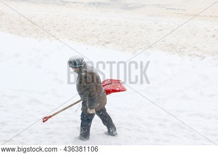 Out Of Focus, Blurry Background. A Masked Man Walks With A Shovel During A Snowfall