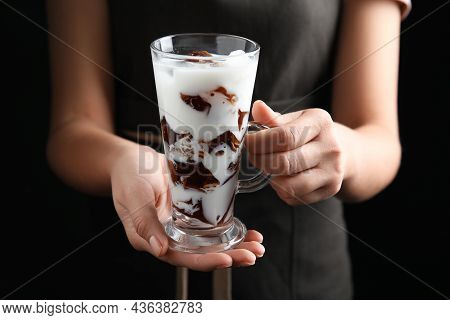 Woman Holding Glass Cup Of Milk With Delicious Grass Jelly On Black Background, Closeup