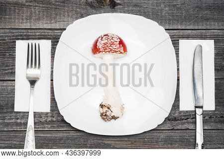 One Red Fly Agaric (amanita Muscaria) On A White Plate With Cutlery Fork And Knife On A Wooden Table