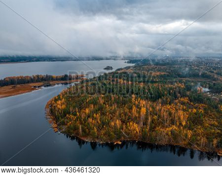Aerial view on island with forest with green and yellow foliage. Low cloudy sky. Autumn landscape of Scandinavian nature. Viborg, Russia. Pure environment.