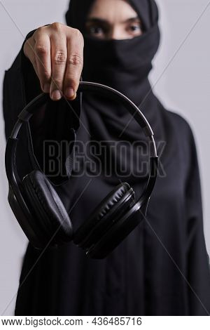 Muslim Woman In Traditional Hijab Clothing Holding Black Wireless Headphones
