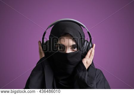 Muslim Woman In Hijab Listening To Music With Wireless Headset. Arabic Girl In Traditional Nikab Clo