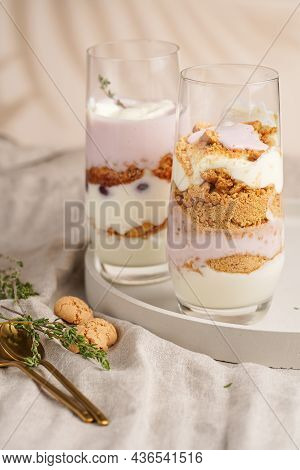 Two Tall Glasses With A Layered Creamy Yoghurt Dessert Trifle With Cookies, Amaretti, Cherries And T
