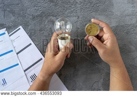 Electricity Costs: Person Checking Electricity Bills With A Light Bulb In One Hand And A Bitcoin In 
