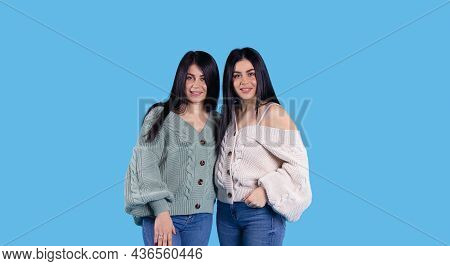 Banner In Long Format On A Blue Background With Two Twin Sisters With Long Black Hair, 20s, Smiling 