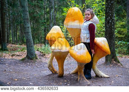 Girl Among Wooden Mushroom Sculptures In The Autumn Forest In Tervete Nature Park, Latvia