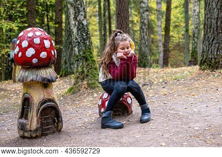 Girl Sitting On A Wooden Mushroom Sculpture In The Woods  In Tervete Nature Park, Latvia