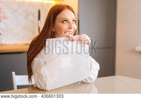 Close-up Face Of Cheerful Young Woman Playing Pops Bubble Wrap To Calm Herself Sitting At Table In K