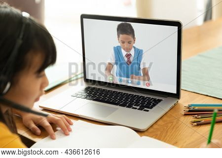 Asian girl using laptop for video call, with elementary school pupil on screen. communication technology and online education, digital composite image.